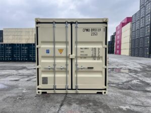 A straight-on, eye-level shot of the closed rear doors of an ivory-colored shipping container in a shipyard. The door features black rubber seals, silver locking bars, and detailed technical specifications printed in dark gray, including the container code "CPWU 090119 1" and "22G3".