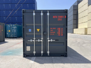 A straight-on, eye-level shot of the closed rear doors of a dark charcoal gray shipping container on a sunny day. The technical details and weight specifications are printed in a bright orange font, featuring the identification code "BETU 330051 4" and "22G3".